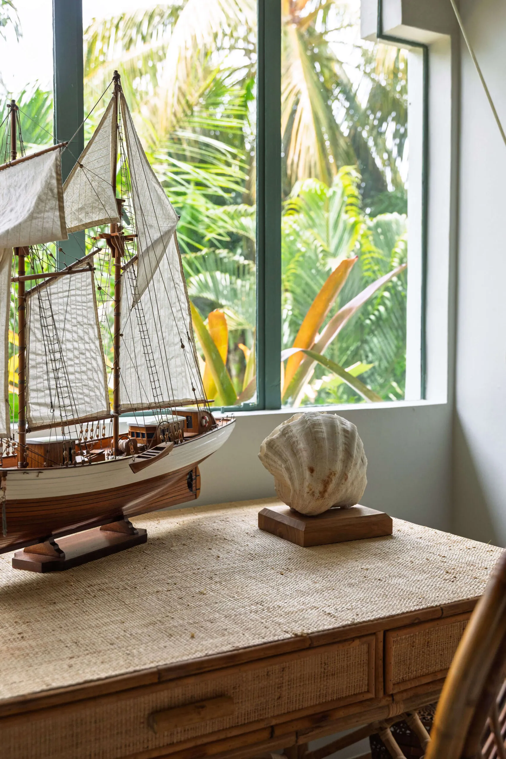 Model sailing ship and a large seashell on a rattan desk by the garden window