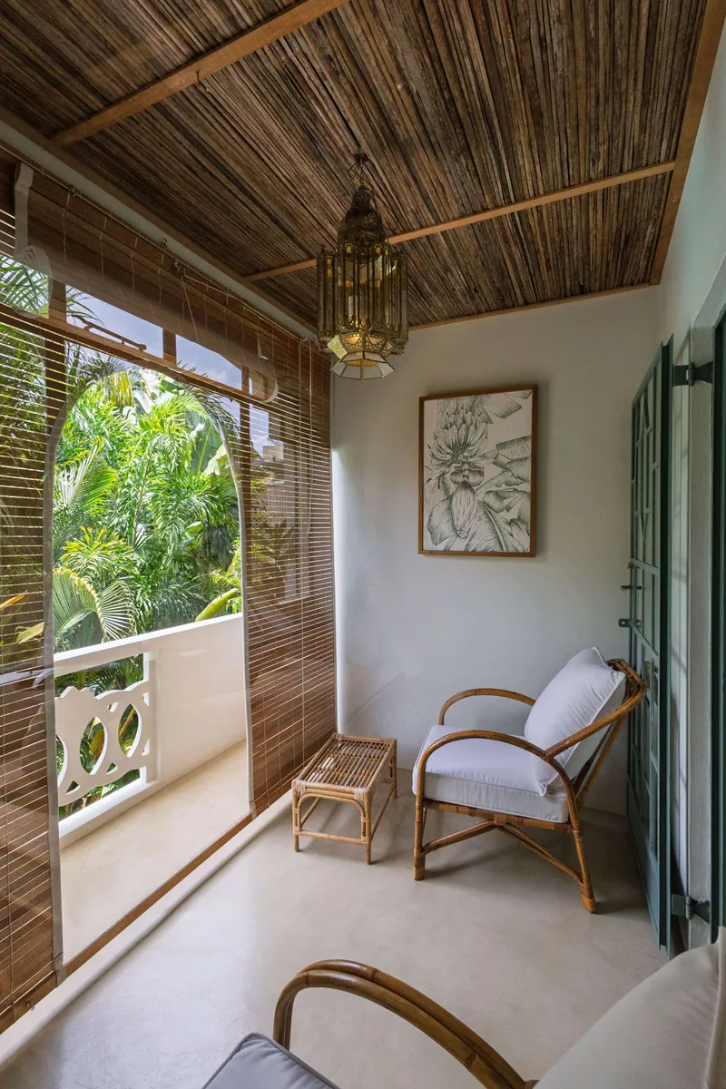 Balcony with a rattan armchair and bamboo blinds, looking onto the palms