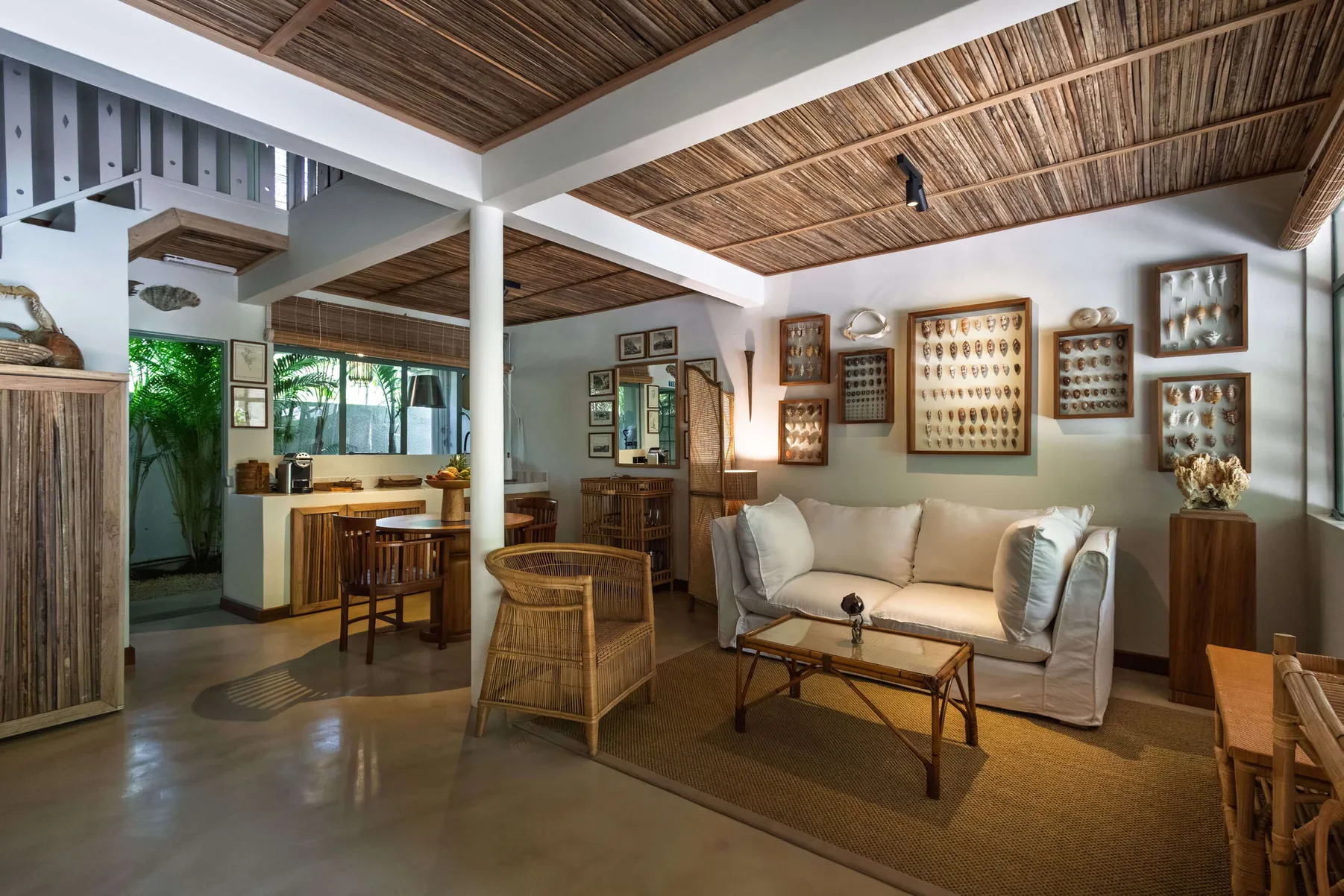 Living room with a white sofa and rattan armchair, open to the dining area