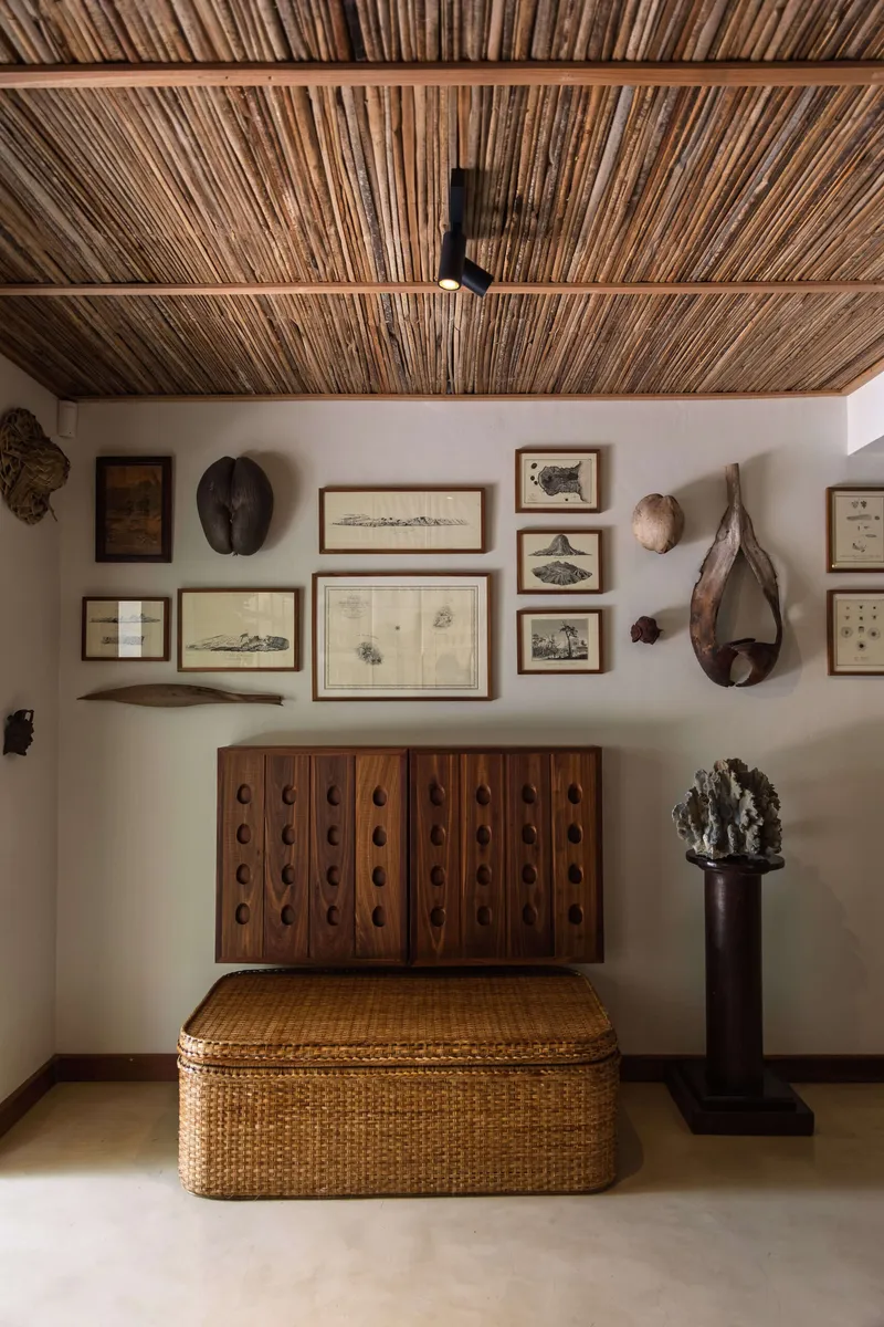 Carved wooden cabinet and woven chest beneath antique maps and prints