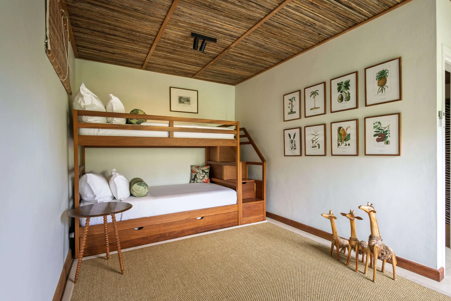 Second bedroom with a wooden bed, giraffe figures and botanical prints